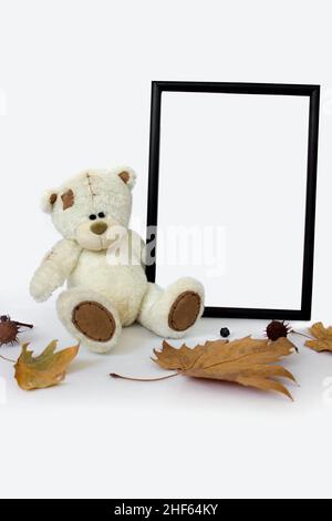 White soft toy bear with vertical frame mockup and autumn leaves with copy space. Empty space. Stock Photo