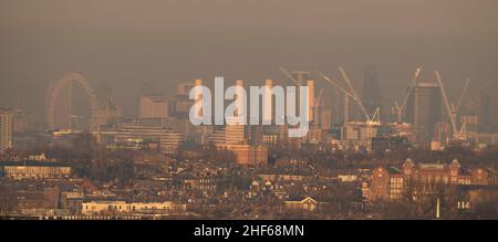 Wimbledon, London, UK. 14 January 2022. Evening sunlight on central London buildings, the London Eye and Battersea Power Station after a day of poor air quality warnings in the capital due to weather conditions. Credit: Malcolm Park/Alamy Live News Stock Photo