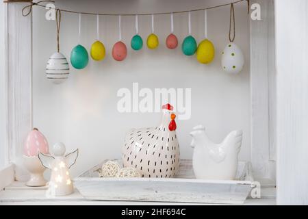 Fragment of the interior. Decorated children's room for Easter. A garland of plastic eggs on the wall. Ceramic hens on the tray on the table. Place fo Stock Photo
