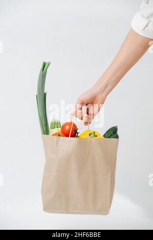 Hand holding grocery paper bag filled with colorful vegetables over white background. Eco friendly compostable products. Stock Photo