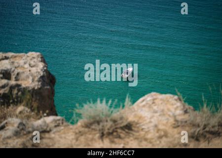 Lonely yacht boat moored in bounty lagoon,  Cape Fiolent in Balaklava,  Sevastopol,  Russia. View from the top of the rock. Azure emerald gree sea water on sunny day. Vacation summer travel concept. Stock Photo