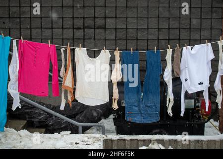 A clothesline of dark and red clothes hangs on a line with two ground sticks and lots of clothespins. The natural way of drying clothes outdoors. Stock Photo