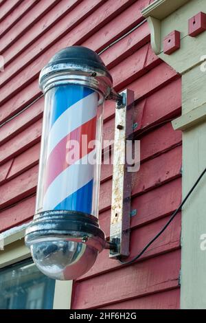 Barbershop pole with red, blue, and white stripes moving around on the outside of a barbershop. The vintage nostalgic pole is attached to a wall. Stock Photo