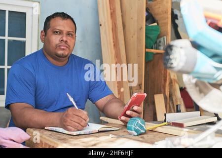 latino man taking notes of the order, in the cabinetry workshop Stock Photo