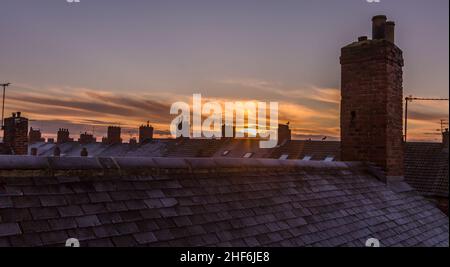 Frost covered roof tiles and chimneys and sunrise in an urban scene Stock Photo