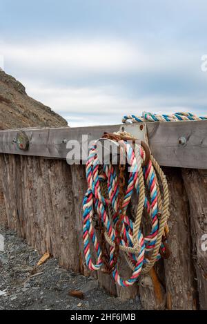 Multiple red, blue, and white braided nylon fishing ropes hanging from a metal hook on a wooden wharf with a blue cloudy sky background. Stock Photo