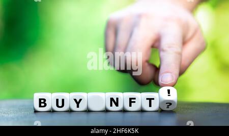 Symbol for buying non fungible token NFT. Hand turns dice and changes the expression "buy NFT?" to "buy NFT!". Stock Photo