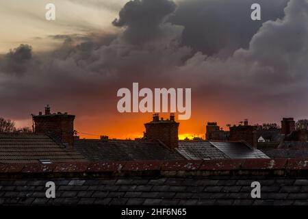 A view across roofs at sunset as a menacing storm cloud looms overhead Stock Photo