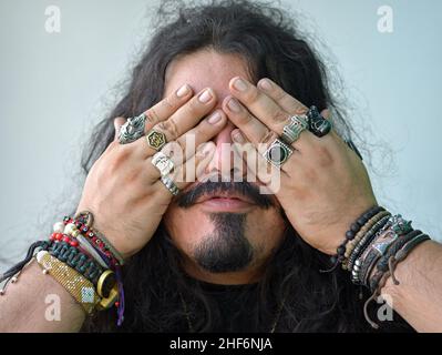 Young Caucasian man with long hair and beringed hands expresses see-no-evil (mizaru) of the proverbial principle of Three Wise Monkeys (one of three). Stock Photo