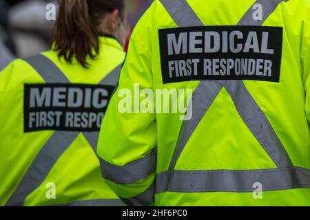 Medical first responders walking along a road wearing black wool stocking caps, yellow reflective coats with the medical first responder in grey. Stock Photo