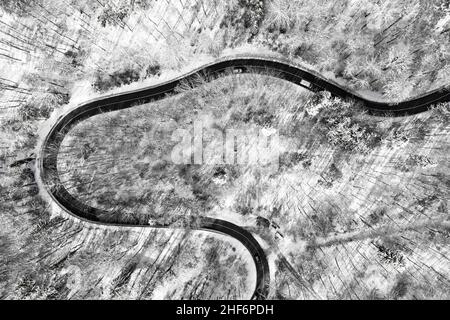 Aerial view at a curvy road as topdown shot in the winter with the street surrounded by the white clean snow Stock Photo