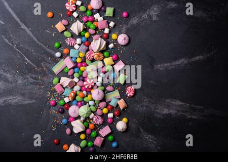 Multicolored sweet and bright dragee, candies, lollipops, marshmallows for fun party on black marble background Stock Photo