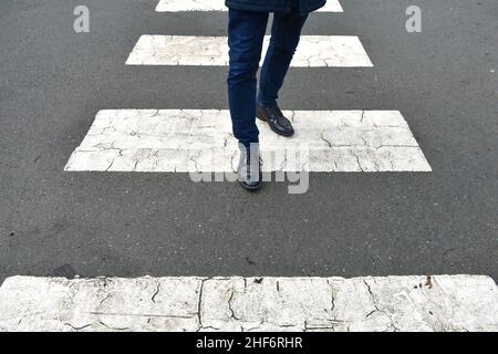 close up of mans feet and legs, walking along a zebra crossing, crossing the road, outside a school in winter Stock Photo