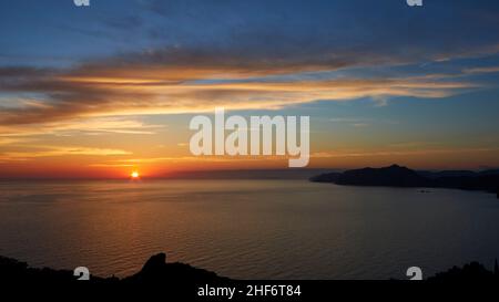 Greece,  Greek Islands,  Ionian Islands,  Corfu,  west coast,  Pentati,  sunset,  view from above to the sea and Agios Gordios (in the shade),  blue sky,  gray clouds,  wide angle view,  coastline in the background,  sun just before setting