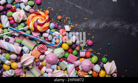 Multicolored sweet and bright dragee, candies, lollipops, marshmallows for fun party on black marble background Stock Photo