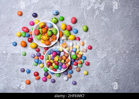 Chocolate multicolored glaze dragee or candies in white bowls on grey concrete background Stock Photo