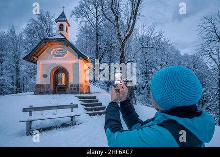 Wiman tourst taking a snapshot of the Kirchleiten-Kapelle at Berchtesgaden in winter,  Berchtesgadener Land district,  Upper Bavaria,  Bavaria,  Germany