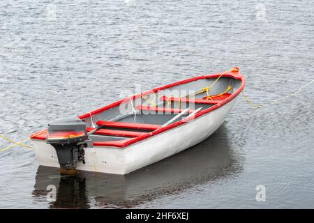 A white wooden boat, fishing boat,  with red trim and interior. The motorboat is moored with a rope. The vessel is reflected in the clear water. Stock Photo