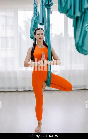 Young beautiful sport woman in orange sportwear practicing yoga. Coach teaching tree pose at gym Stock Photo