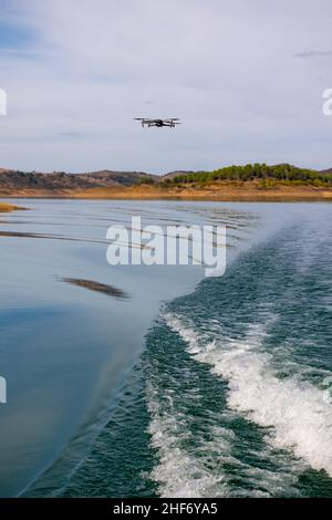 View of drone with camera flying over water with a wave forming in the foreground. Stock Photo