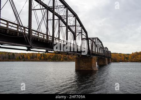 Steel trestle bridge with wooden deck over a large river in Newfoundland.  The bridge is for foot traffic and ATV usage. The sky is clear blue. Stock Photo