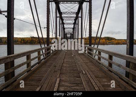 Steel trestle bridge with wooden deck over a large river in Newfoundland.  The bridge is for foot traffic and ATV usage. The sky is clear blue. Stock Photo