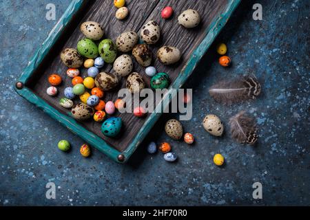 Top view of small quail eggs and bright candies for Easter day in old rustic turquoise wooden box on blue concrete background Stock Photo