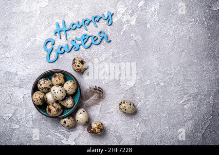 Top view of small quail eggs in bowl and blue text of Happy Easter on grey concrete background Stock Photo