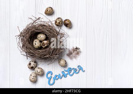 Small quail eggs as symbol of Easter day in bird nest as traditional decoration on white wooden background Stock Photo