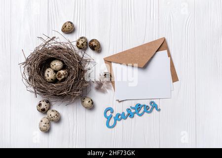 Small quail eggs as symbol of Easter day in bird nest as traditional decoration and mock-up of blank card on white wooden background Stock Photo