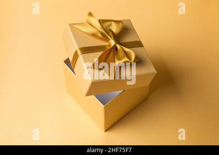 Beautiful golden square gift box with shiny satin bow for christmas or birthday presents on gold background Stock Photo