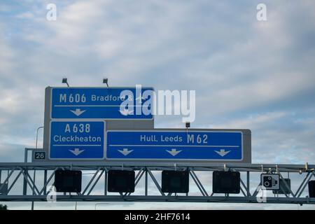 Blue British motorway sign above motorway directing transport towards Leeds, Bradford, Hull and Cleckheaton. Speed camera plaques also visible. Space Stock Photo
