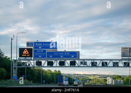 Leeds, UK - 19th June 2019: Blue British motorway sign above motorway directing transport towards Leeds, Bradford, Hull and Cleckheaton. Electronic si Stock Photo