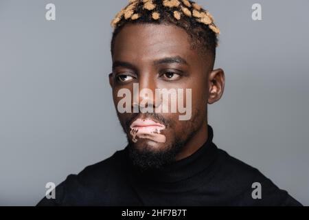 portrait of young african american man with vitiligo and trendy hairstyle isolated on grey Stock Photo