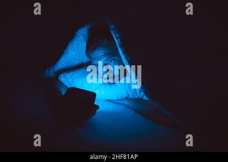 Young man lying in bed and using smartphone before sleep. Social media addiction and insomnia Stock Photo