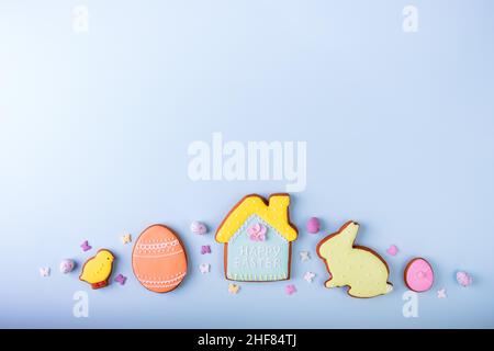 Easter greeting card with colorful rabbits, eggs, chickens gingerbread cookies on blue background with copy space. Mock up. Banner. Top view. Stock Photo
