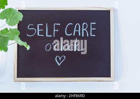 Blackboard with self care o'clock written with chalk with plant to the side Stock Photo