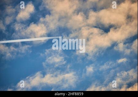 Airplane with contrails behind clouds in the blue sky in the evening,  Bavaria,  Germany Stock Photo