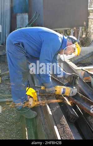 older man with angle grinder cutting up scrap steel Stock Photo