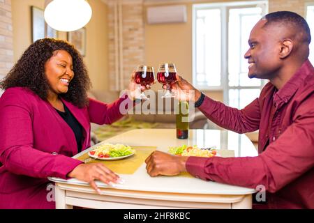 Authentic people african american couple in love drinking wine from glasses and eating italian pasta in living room 14 february valentines day Stock Photo