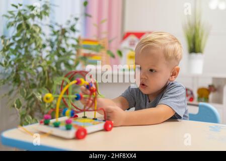 little boy child blonde play with toy to sit at the table at home Stock Photo
