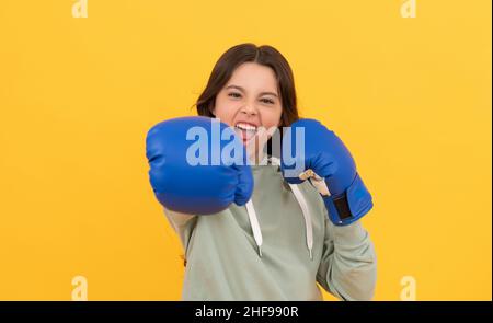 aggressive child punching in boxing gloves on yellow background, sport Stock Photo