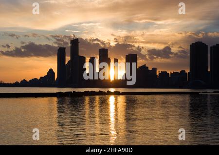 Amazing sunset over sityscape. Cloudy sky with sun rays, lake water reflection. City downtown modern buildings. no people Stock Photo