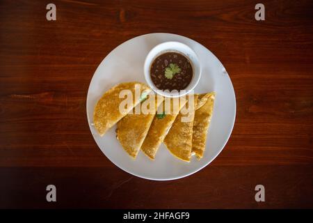 Plate with traditional quesadillas and cup of beans on brown table Stock Photo