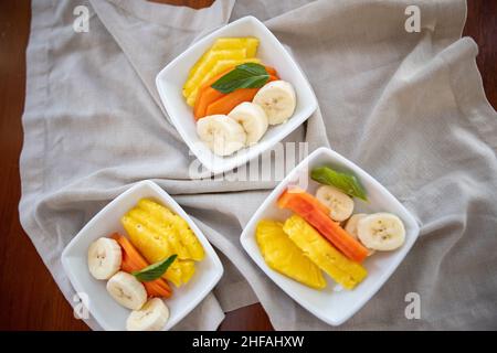 Square plates with fresh fruit slices on wrinkled gray napkin Stock Photo