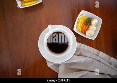 Cup of coffee and small plate with fresh fruit slices on brown table Stock Photo
