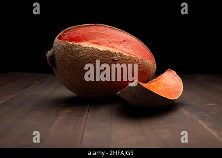 still life image of one mexican red mamey close up on rustic wooden surface and black background Stock Photo