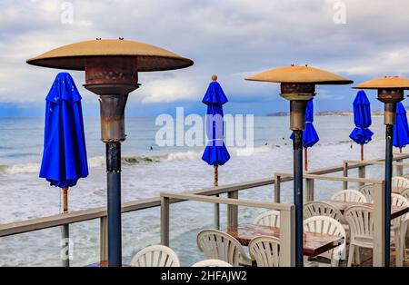 Blue umbrellas and outdoor heaters at a cafe on the beach with Pacific Ocean waves below in a famous tourist destination, San Clemente California, USA Stock Photo