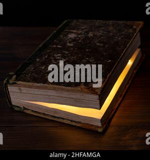 A glow of light inside an ancient closed book on a wooden table Stock Photo