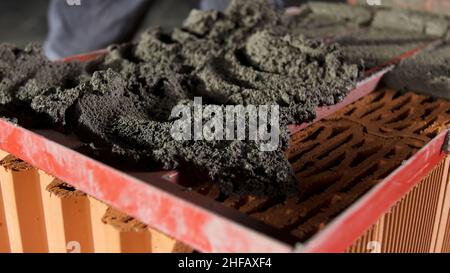 Bricklayer putting down raw cement and making an even layer to put another brick on it. Close up of making a brick wall process. Stock Photo
